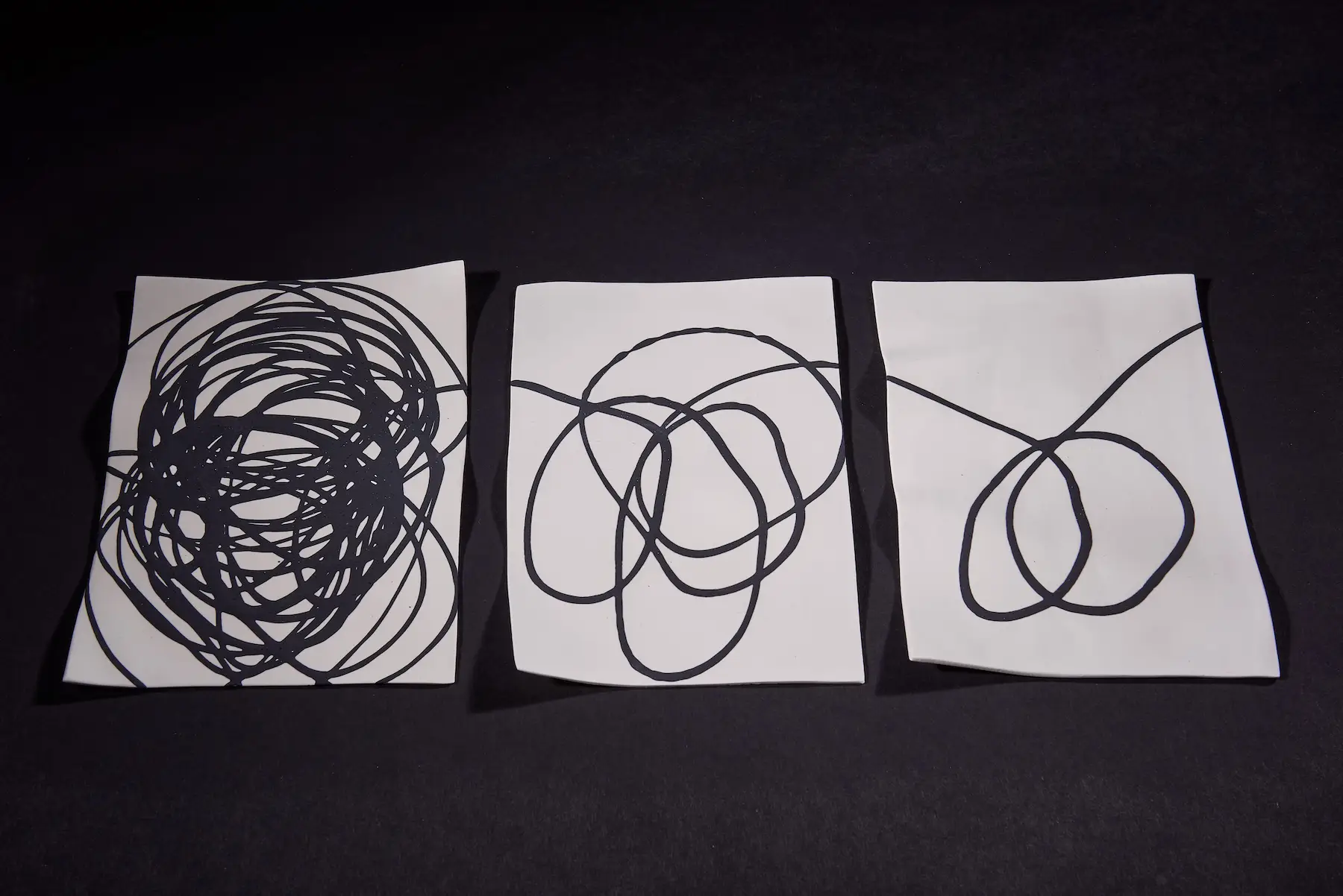 Scribble, Triptych — Screwed Up, black stoneware scribble form displayed above porcelain sheets. Studio Willis.